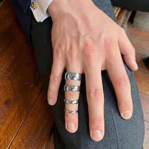 Puede incluir: Un conjunto de cuatro anillos de metal plateado pulido usados en un solo dedo. Los anillos est&aacute;n apilados verticalmente, cada uno con un dise&ntilde;o de banda lisa y redondeada con una superficie reflectante que capta la luz de manera uniforme.