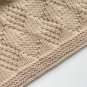 May include: A white ceramic mug with a black handle and the text "But First, Coffee" in a bold, black font. The mug is set against a blurred background, suggesting a cozy setting.