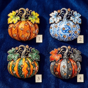 May include: Four pumpkin-shaped brooches with metallic stems and leaves, each adorned with amber-colored rhinestones. Number 1 is orange, 2 is blue and white floral, 3 is green and orange, and 4 features orange and black scrollwork patterns.