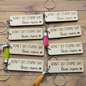 Puede incluir: Seis llaveros de madera con borla. Cada llavero tiene grabado el texto "DON'T DO STUPID SHIT. love, mom". Los llaveros son de varios colores, incluyendo rosa, verde y naranja.