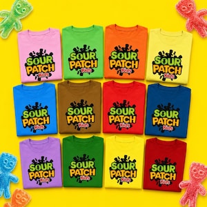 May include: A collection of twelve short-sleeved t-shirts in various solid colours including pink, green, orange, yellow, blue, brown, red, purple, and dark green, each featuring the black and green Sour Patch Kids logo printed on the front.