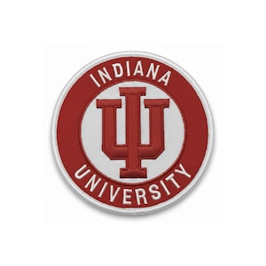 May include: A round embroidered patch featuring the Indiana University logo. The logo is a stylized letter "I" with a "U" shape inside. The patch has a red border with the words "INDIANA UNIVERSITY" in white.