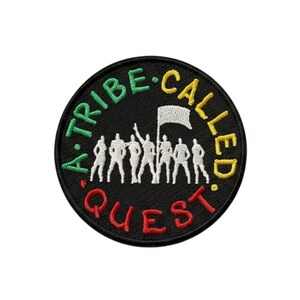 May include: Embroidered patch with the text "A Tribe Called Quest" in green, yellow, and red. The patch features a silhouette of people holding a flag on a black background. A circular patch.