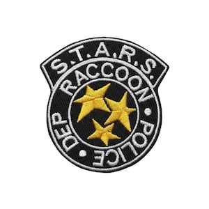 Op de afbeelding: Een zwart-wit geborduurde patch met de tekst "S.T.A.R.S. RACCOON POLICE DEP" en drie gele sterren. De patch heeft een schildvorm en is bedoeld voor kleding of accessoires.