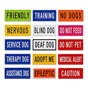 May include: A collection of rectangular dog tags with various text labels in white font on colored backgrounds. The tags include phrases like "Friendly," "Training," "No Dogs," and "Service Dog."
