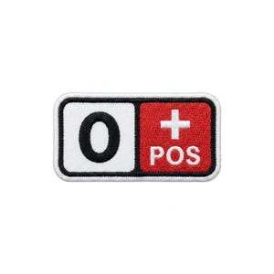 以下が含まれることがあります： 白い縁取りのある長方形のパッチ。左側は白で黒の「0」があります。右側は赤で、文字「POS」の上に白い「+」記号があります。