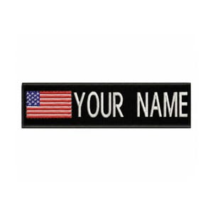 Può includere: Una toppa ricamata nera con la scritta "YOUR NAME" in lettere maiuscole bianche. La toppa presenta una piccola bandiera americana sul lato sinistro, con strisce rosse e bianche e un campo blu di stelle.