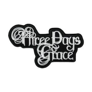 May include: Black and white embroidered patch featuring the text "Three Days Grace" in a stylized font. The patch has a black background with white lettering and a white border. The patch is likely for a jacket or bag.