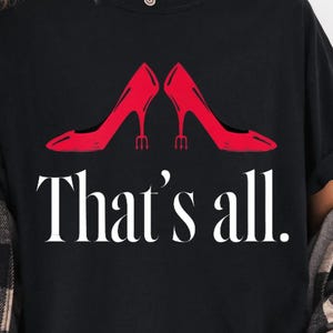 May include: Black t-shirt featuring a pair of red high heels and the text "That's all." The design is printed in white. The shirt is worn with a black and white plaid shirt.