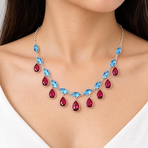 May include: A silver-toned necklace featuring a series of marquise-cut light blue stones arranged in a chain, with dangling teardrop-shaped deep red stones suspended from the blue stone settings, secured by a thin silver-toned metal chain.