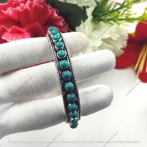 May include: A silver cuff bracelet featuring a single row of eleven round, polished turquoise stones set in a vertical line. The bracelet is framed by two twisted silver rope borders that run along the length of the band, creating a textured edge.