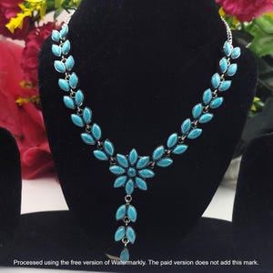 May include: A silver-toned necklace featuring a series of marquise-shaped turquoise-coloured stones arranged in a leaf-like pattern. The design culminates in a central flower motif with a dangling vertical drop of matching leaf-shaped stones.