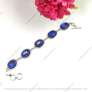 Può includere: Un bracciale a maglie color argento con cinque pietre blu ovali sfaccettate incastonate in cornici di metallo. Il bracciale presenta una chiusura a T a un'estremità e una serie di anelli di regolazione circolari, con filigrana.