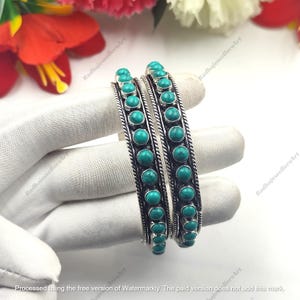 Puede incluir: Dos brazaletes de plata con una hilera de piedras redondas de color turquesa en el centro. Cada brazalete está bordeado por un diseño de metal trenzado en forma de cuerda a ambos lados, creando una apariencia texturizada a lo largo.