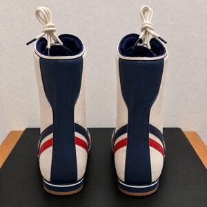 Rear view of a pair of custom high-top wrestling boots highlighting the blue heel strips, red side accents, and knotted white laces.