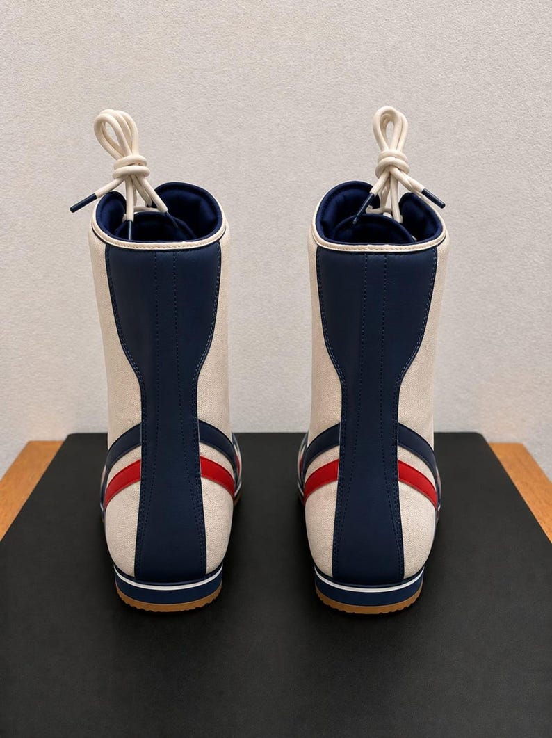 Rear view of a pair of custom high-top wrestling boots highlighting the blue heel strips, red side accents, and knotted white laces.
