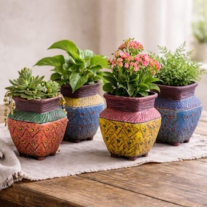 May include: Four decorative ceramic planters with colorful geometric designs. Each pot holds a different plant, including succulents and flowering plants. The pots are in shades of orange, yellow, blue, and green, with a textured finish.