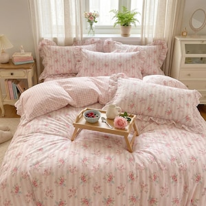 Może przedstawiać: Łóżko z pościelą w różowo-białe kwiaty. Poszwa na kołdrę i poduszki mają wzór w paski i kwiaty. Drewniana taca zawiera miskę z jagodami, dzbanek i różę.