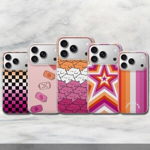 Könnte beinhalten: Fünf Smartphone-Hüllen mit verschiedenen Designs: ein pink-orangefarbenes Karomuster, ein hellrosa Hintergrund mit kleinen illustrierten Dosen, ein sich wiederholendes Muster aus Katzengesichtern, eine große Stern-Grafik und vertikale Streifen mit dem Text LOVE IS LOVE.