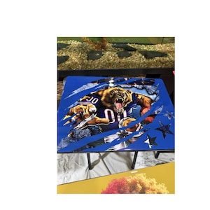 May include: A blue table with a graphic of a bear tearing through a blue background, revealing a football player. The bear is wearing a football uniform with the number 01. The table has black legs and is decorated with star shapes.