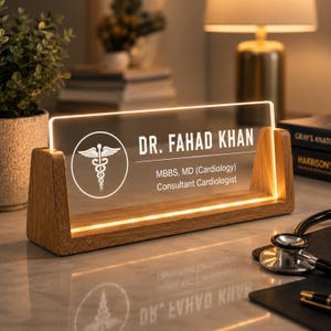 May include: A lighted desk nameplate with the text "DR. FAHAD KHAN" and medical credentials. The nameplate is clear with a white medical symbol and text, set in a wooden base. A stethoscope and books are in the background.