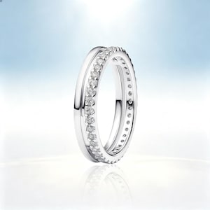 May include: A silver-toned ring featuring a smooth, polished band alongside a second, thinner band encrusted with a continuous row of small, clear, round-cut stones. The two bands are connected, creating a layered, dual-band appearance.
