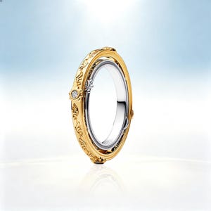 Könnte beinhalten: Ein zweifarbiger Ring mit einer polierten silberfarbenen Innenschiene und einer drehbaren goldfarbenen Außenschiene. Der goldene Ring ist mit komplizierten Gravurmustern und einem einzelnen kleinen, klaren, rund geschliffenen Edelstein in einer runden Fassung verziert.