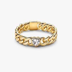 Puede incluir: Un anillo de eslabones en tono dorado con una piedra preciosa transparente en forma de corazón en el centro. La banda está construida con eslabones metálicos entrelazados con un acabado pulido y liso, e incluye un segmento rectangular plano.