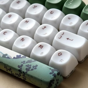 Może przedstawiać: Biały ceramiczny kubek z czarnym uchwytem i napisem "But First, Coffee" czarną, pogrubioną czcionką. Kubek stoi na białej powierzchni. Kubek ma około 10 cm wysokości.