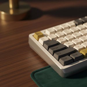 May include: A mechanical keyboard with white, grey, and yellow keycaps. The keyboard is on a wooden surface with a green mat. The keycaps are arranged in a QWERTY layout. The keyboard has a modern, minimalist design.