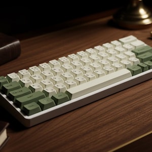 May include: A mechanical keyboard with a white and green keycap colour scheme. The keyboard has a rectangular shape with a white frame. The keycaps are a mix of off-white and green. The keyboard is on a wooden surface.