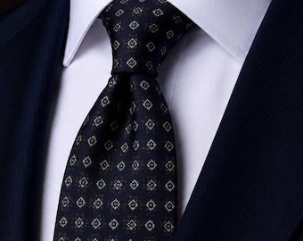 Puede incluir: Una corbata azul marino oscuro con un patrón geométrico repetitivo de pequeños rombos blancos y gris claro. La corbata está anudada sobre una camisa de vestir blanca de cuello rígido, que se lleva debajo de una chaqueta de traje azul marino.