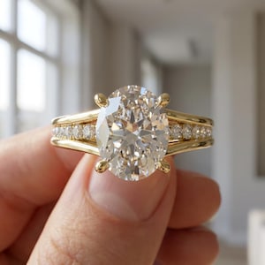 Pode incluir: Um anel de noivado dourado com um grande diamante de corte oval. A banda é adornada com diamantes menores. O anel é exibido, destacando seu design e brilho. O estilo é clássico e elegante. Uma joia de luxo.