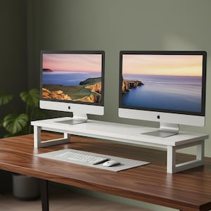 May include: Two silver computer monitors with a scenic landscape display sit on a white monitor stand. A keyboard and mouse are on a gray mat in front of the monitors. The desk is made of dark wood.