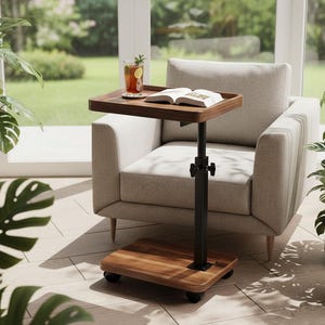 May include: A wooden side table with a dark brown tray and a black adjustable stand. The table has a square base with wheels. A drink and a book rest on the tray, next to a light-colored armchair. Plants in white pots are in the background.