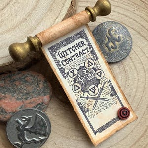 Könnte beinhalten: Eine Schriftrolle mit der Aufschrift Witcher Contract, schwarzen Tuschezeichnungen von Schwertern und Symbolen sowie goldfarbenen Holzenden. Dazu gehören zwei runde Metallmünzen, eine mit einem Drachenrelief und eine mit einem Symbol, sowie ein Stein.