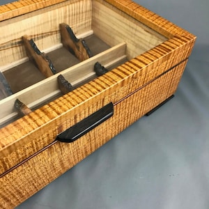 May include: A wooden box with a glass top and a black handle. The box has a wood grain pattern and is divided into compartments.