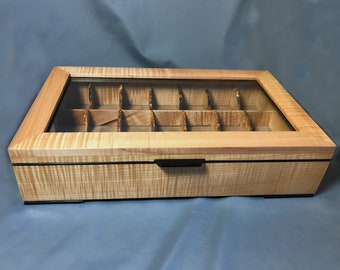 May include: A wooden box with a glass top and a black handle. The box has 16 compartments and is made of maple wood.