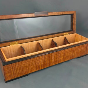 May include: A wooden box with a glass top and five compartments. The box is made of light and dark wood with a natural wood grain pattern.