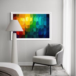 May include: A framed abstract art print with a vibrant, colorful design. The artwork features a pattern of overlapping semi-circles in shades of red, orange, yellow, green, and blue. The print is displayed above a gray armchair with a patterned pillow.