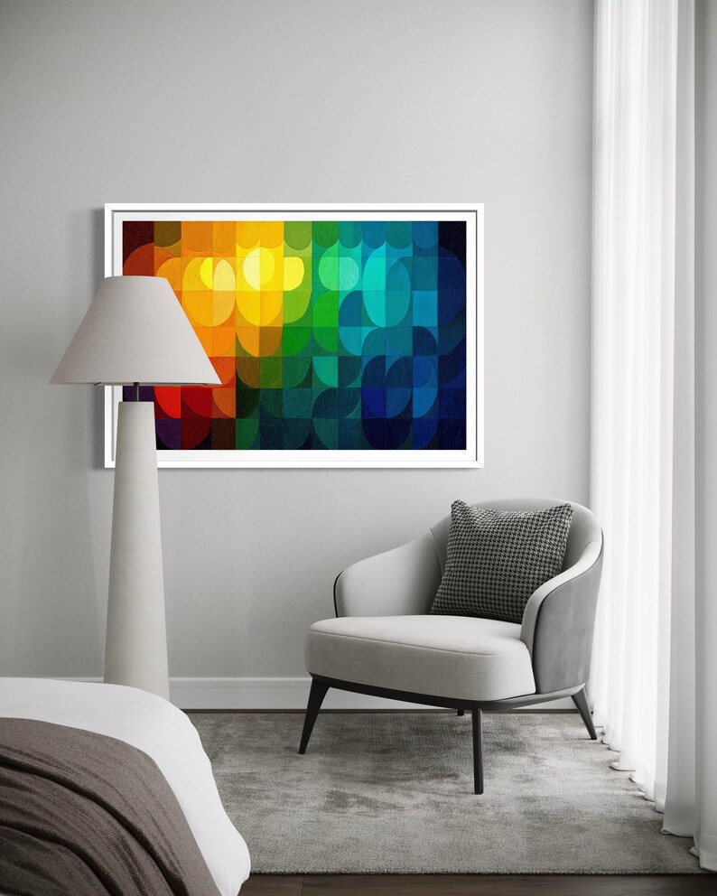 May include: A framed abstract art print with a vibrant, colorful design. The artwork features a pattern of overlapping semi-circles in shades of red, orange, yellow, green, and blue. The print is displayed above a gray armchair with a patterned pillow.