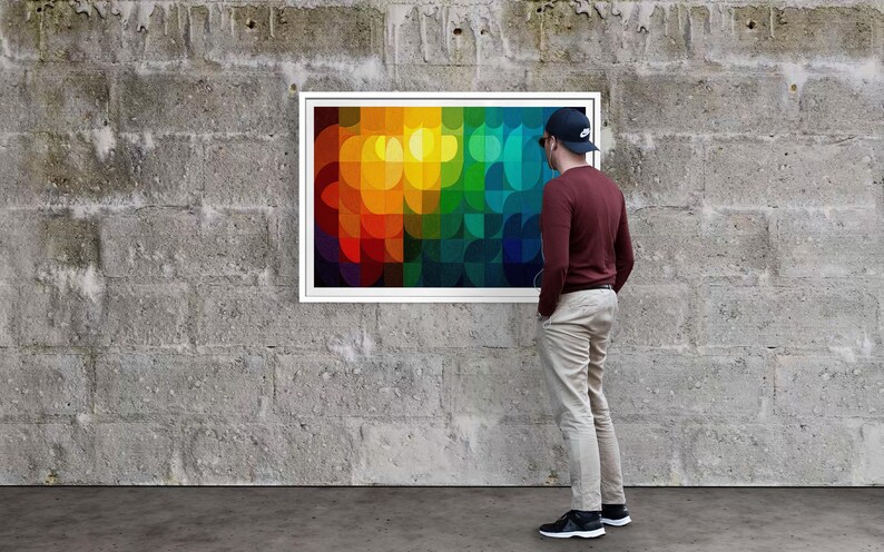 May include: A framed abstract art piece with a vibrant, colorful design of overlapping shapes in shades of red, orange, yellow, green, and blue. The artwork is displayed on a gray concrete wall.