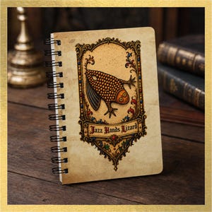 May include: A spiral-bound notebook with a beige, parchment-style cover featuring an ornate, gold-toned frame. Inside the frame is a textured, orange-spotted lizard illustration and the text "Jazz Hands Lizard" in a black gothic font.