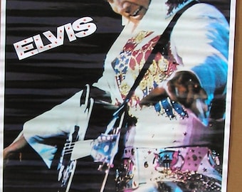 May include: Poster of Elvis Presley in a white jumpsuit with star and jewel detailing, playing a guitar. The word "ELVIS" is in white letters with red stars. The background is dark.