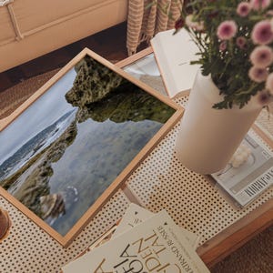 Pode incluir: Uma caneca de cerâmica branca com uma alça preta e o texto "But First, Coffee" em estilo manuscrito. A caneca está sobre uma superfície branca. A caneca tem aproximadamente 10 cm de altura.