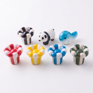 Peut inclure: Un ensemble de sept repose-baguettes en céramique comprenant cinq repose-baguettes en forme de fleur avec des rayures verticales noires, rouges, jaunes, bleues et vertes, ainsi qu'une figurine de panda noir et blanc et une baleine bleue et blanche.