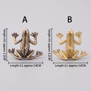 May include: Two metal frog figurines labeled A and B. Frog A has a dark bronze finish, while frog B has a bright gold finish. Each frog measures approximately 3.2 cm in height and 3.8 cm in length. Both frogs are depicted in a flat, splayed position.