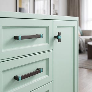 Peut inclure: Un meuble vert menthe clair dot&eacute; de deux poign&eacute;es de tiroir rectangulaires horizontales et d'un bouton de porte en forme de T. La quincaillerie est brun fonc&eacute; avec des accents en pierre turquoise vive aux extr&eacute;mit&eacute;s et au centre.