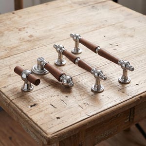 May include: A collection of four cabinet hardware pieces featuring a combination of polished silver-tone metal bases and cylindrical brown wood grips. The set includes one T-shaped knob and three varying lengths of drawer pulls with rounded ends.