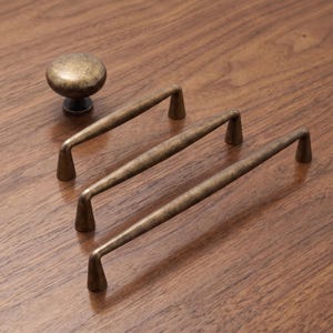 May include: A set of antique brass hardware consisting of one round cabinet knob and three elongated drawer pulls. Each piece features a weathered, dark metallic finish with a smooth, rounded profile and tapered mounting points for attachment.